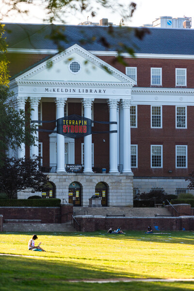 Terrapin Strong mask banner on the front exterior of McKeldin Library at dusk; Testudo statue in the foreground.